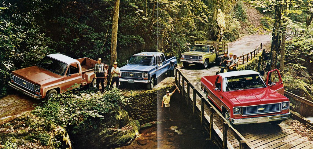 Una foto del folleto de camionetas Chevy del 1973 original con cuatro pickups de la serie C/K juntas en un camino de tierra y puente de madera junto a una colina empinada cubierta de árboles.