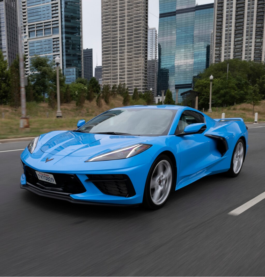 Un Corvette azul brillante circula por un camino con rascacielos de fondo.