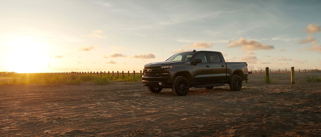 Una Silverado LT Trail Boss en Gris se encuentra en un lugar de estacionamiento iluminada desde el fondo con la luz del sol naciente.