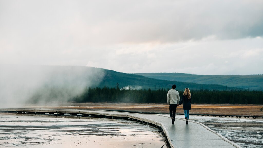 Dos personas caminan por una pasarela de Yellowstone, un vapor emanado de un estanque caliente a su izquierda.