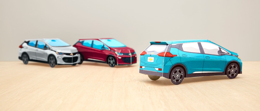 Tres modelos de papel terminados del Bolt EV en Plata Hielo Metálico, Rojo Cajún y Azul Oasis sobre una mesa.