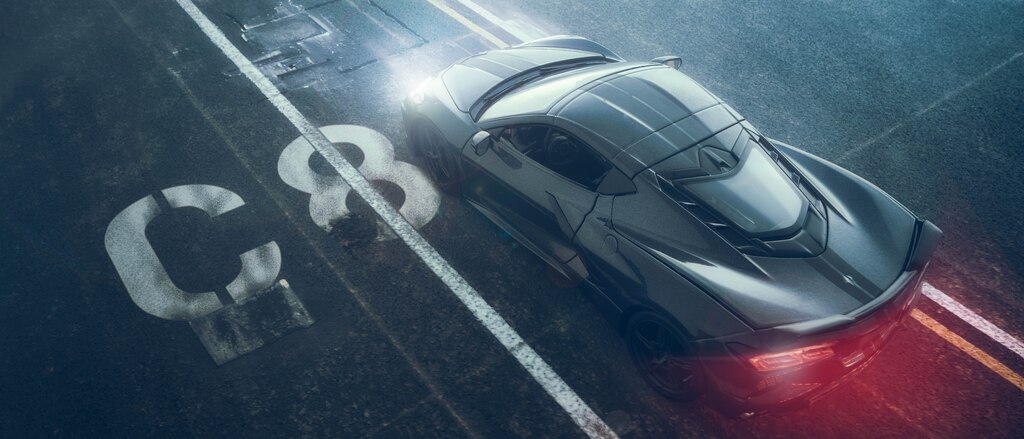 Un Corvette Stingray negro en miniatura visto desde arriba y con un brillo rojo proveniente de sus faros traseros, que parece estar moviéndose, con pavimento negro y marcas de carril de fondo, y con un esténcil de "C8" en blanco al lado del auto.