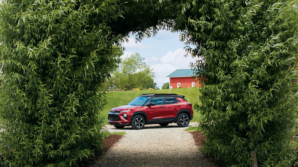 La Chevi Trailblazer RS enmarcada por un arco cubierto de vegetación, con estructuras agrícolas de fondo.
