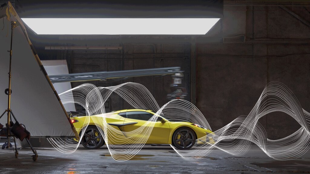 Un Corvette Z06 amarillo se encuentra en un tipo de edificio de almacén frente a un fondo oscuro y brillantemente iluminado desde el frente. Las ondas de sonido ilustradas se entrelazan alrededor del automóvil.