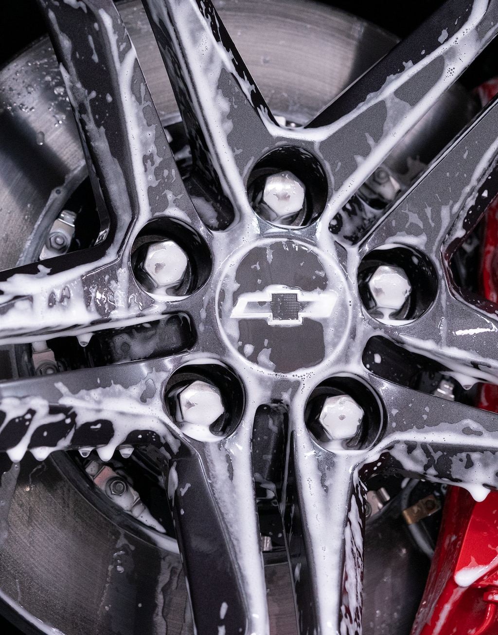 Primer plano en detalle de un rin de cinco brazos en un Chevy Camaro rociado con gotas de espuma blanca.