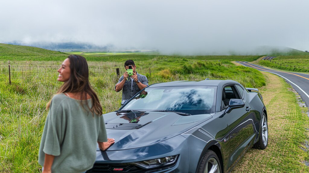 Un hombre usa una cámara Polaroid para tomar una foto de una mujer cerca del frente de un Camaro SS 2020.