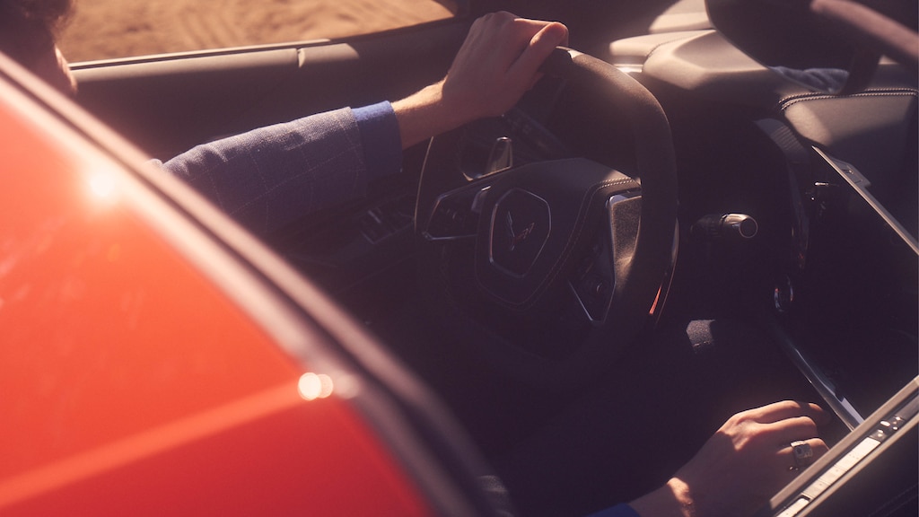 Una vista de la cabina del Corvette
2020 a través del techo abierto. Hay una persona en el asiento del conductor y la foto muestra solo una mano en el volante y la otra en la palanca de cambios.