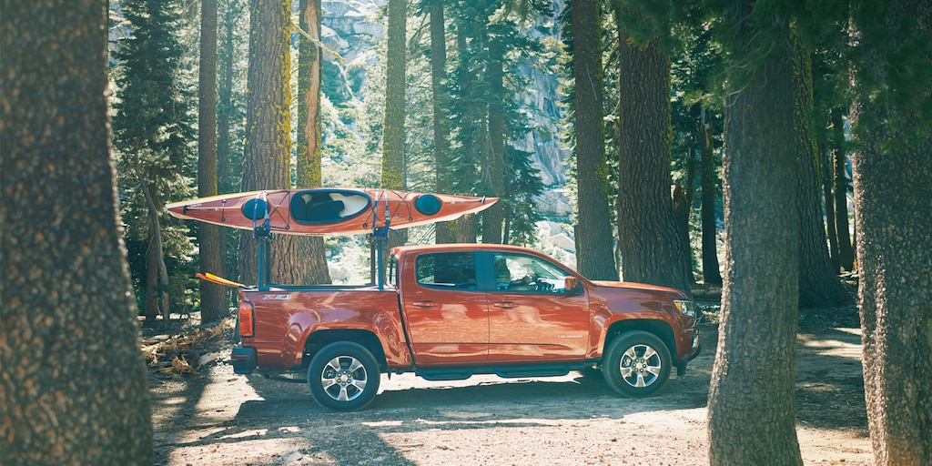 Una Chevy Colorado con dos kayaks en el soporte para equipos, atravesando un bosque.