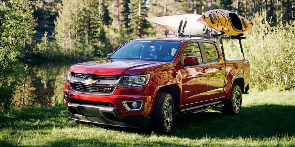 Una Chevy Colorado con dos kayaks sobre un soporte, estacionada cerca del bosque.