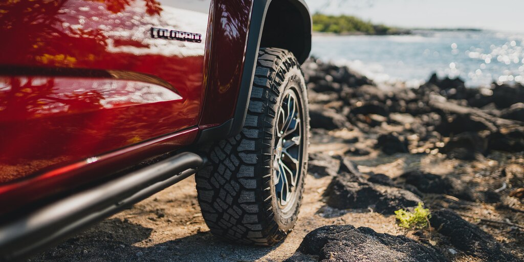Primer plano de un neumático de una Chevrolet Colorado ZR2 sobre un terreno rocoso y con el mar de fondo.