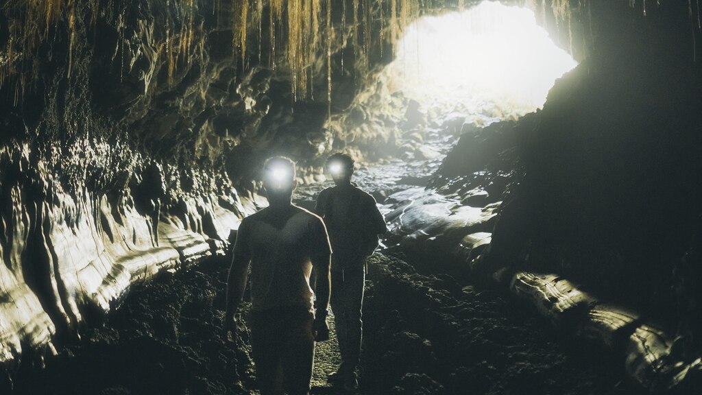 Dos hombres usando lámparas mineras exploran el interior de las cuevas Kaumana.