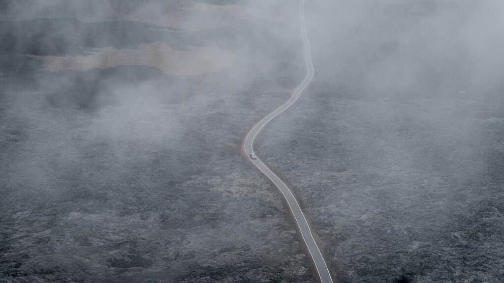 Una toma desde un dron de una porción de carretera serpenteante a través de un campo de lava negro, vista a través de la bruma.