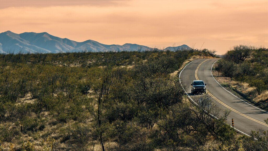 Una Tahoe RST en Negro andando por un camino sinuoso, con montañas de fondo. El sol se está poniendo y hace que las nubes y el cielo detrás de las montañas adquieran un color melocotón.