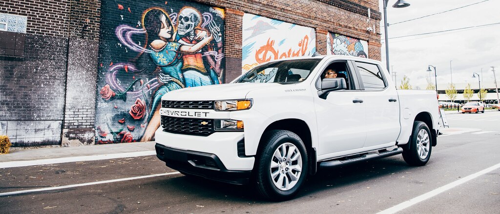 Freddy Diaz en una Silverado blanca en una calle de Detroit junto a uno de los coloridos murales de Freddy.