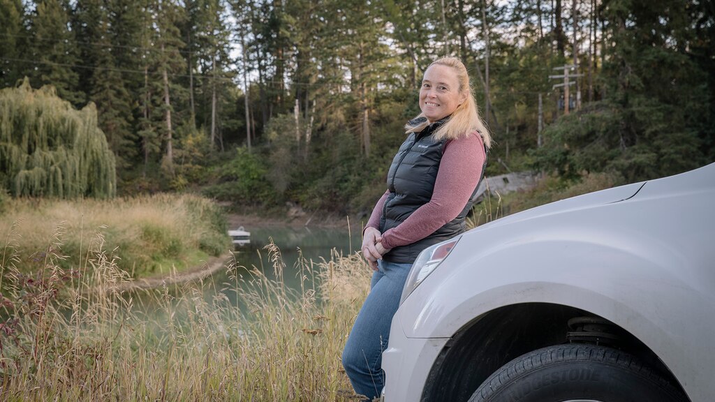 Jennifer, miembro de OnStar, apoyada sobre el frente de su camioneta con un campo y árboles en el fondo.