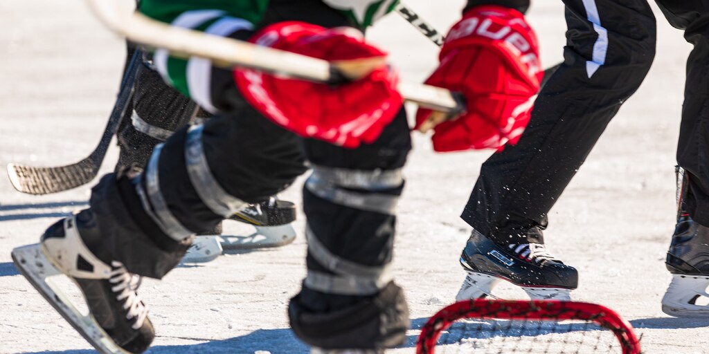 Primer plano de un jugador completamente equipado que lleva un palo en las manos y patina sobre el hielo.