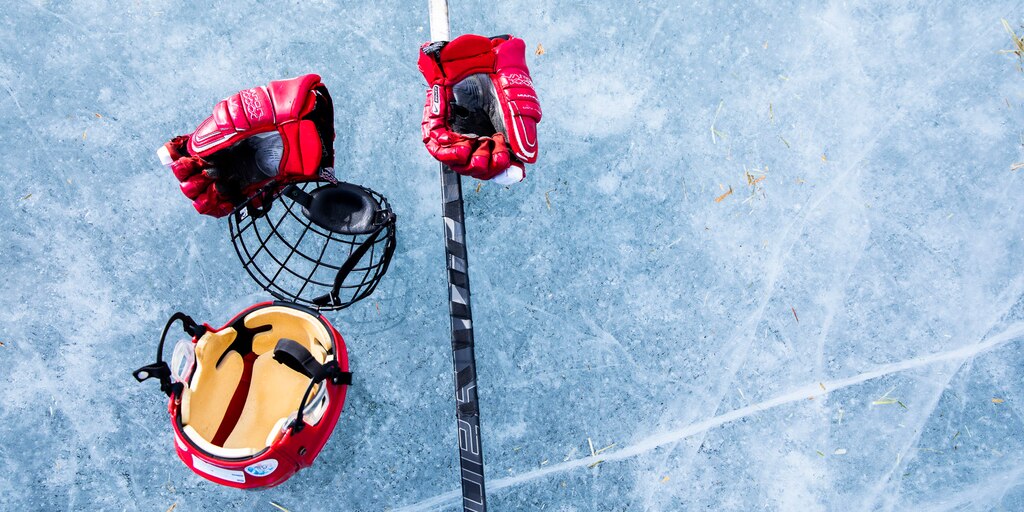 Un par de guantes de hockey, un casco, protección facial y un palo sobre el hielo.