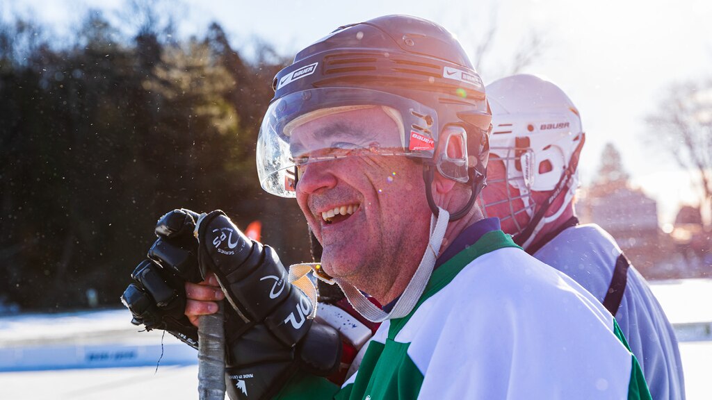 Un hombre con un casco y guantes de hockey que sostiene un palo de hockey y sonríe.