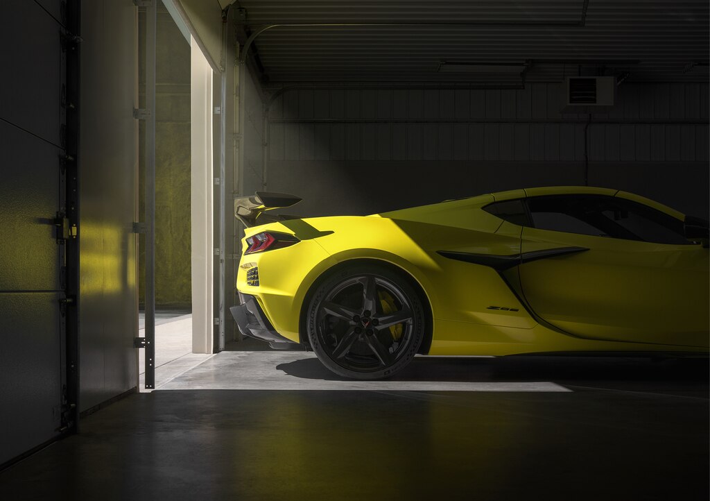 La parte trasera de un Corvette Z06 amarillo, iluminada por una puerta de garaje abierta detrás.