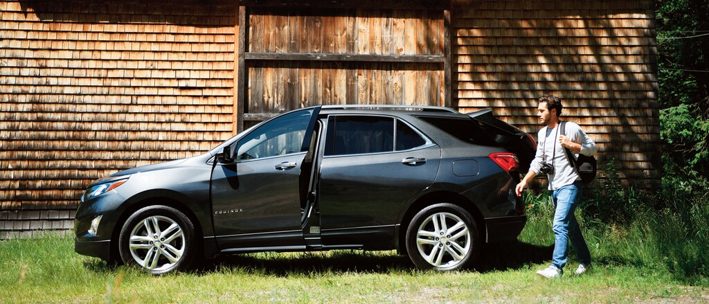 Un hombre con una cámara pasando por una Chevrolet Equinox en frente de una antigua casa de tejas de madera.
