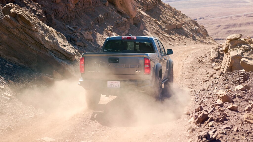 Una Chevy Colorado ZR2 Bison gris vista desde atrás en un camino de tierra con rocas rojas a ambos lados.