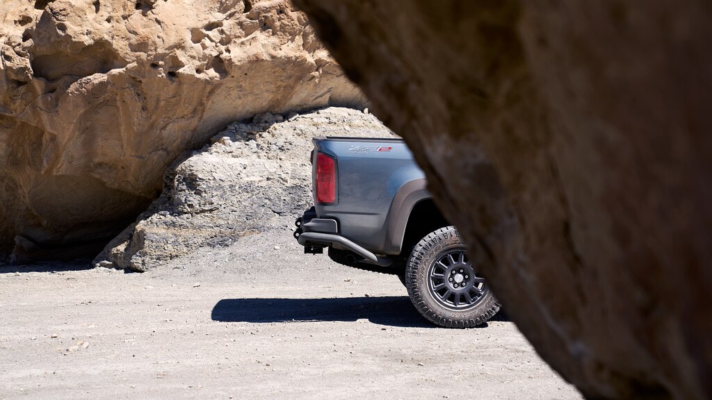 Parte trasera de una pickup Chevy Colorado ZR2 gris vista en un camino de tierra, detrás de una formación de rocas rojas.