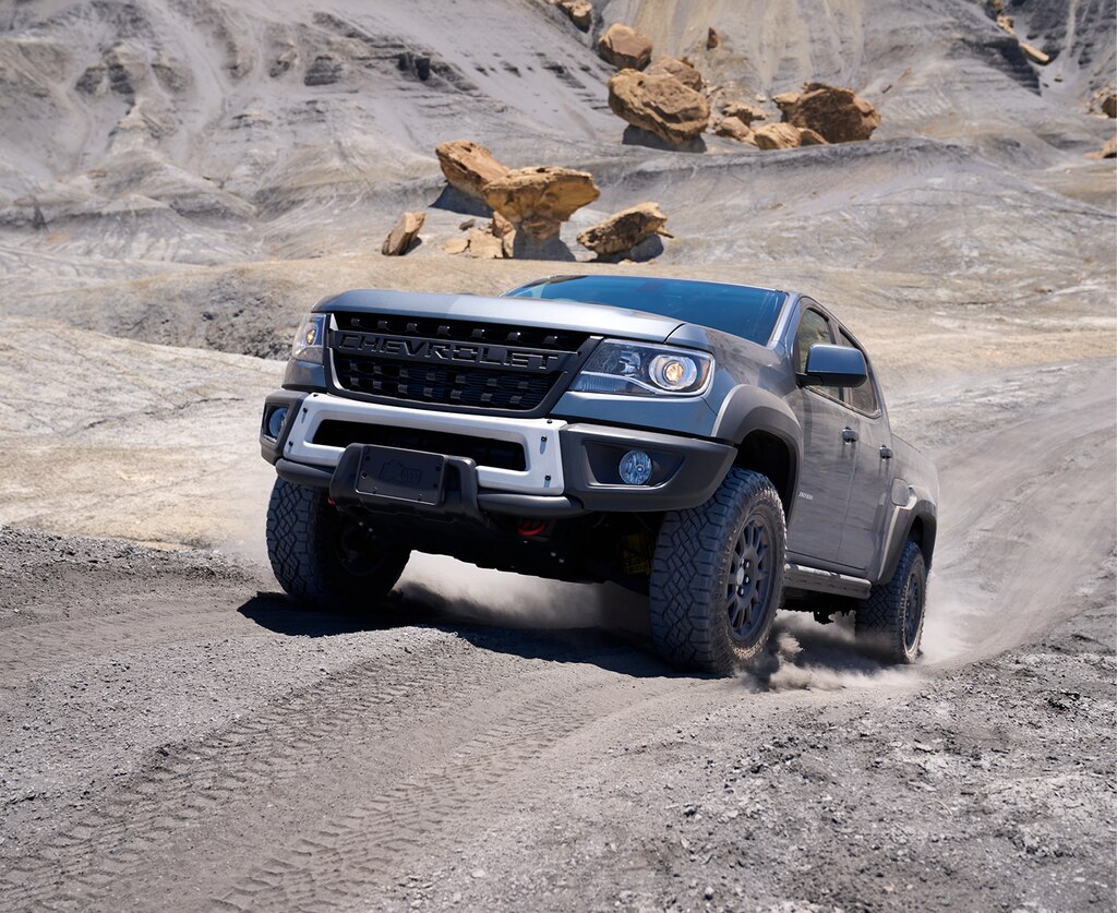 Una Chevy Colorado ZR2 Bison gris trepando una pendiente pronunciada en un camino de tierra, con rocas rojas de fondo.