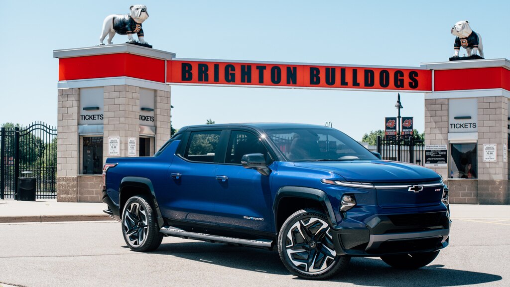 Una Silverado EV Azul en un estacionamiento frente a la entrada a un estadio. Un cartel que dice Brighton Bulldogs con la estatua de un perro bulldog a cada lado de la entrada.