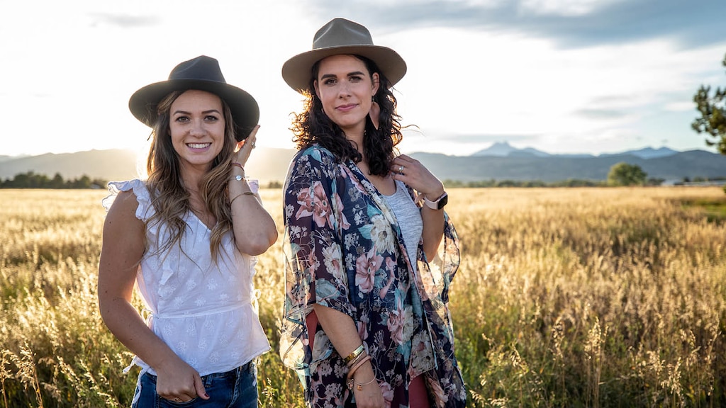 Brittany y Courtney McLachlan posan con sombreros, con un campo y montañas a la distancia en el fondo.