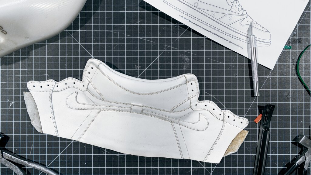 Una horma, piezas de diseños para un tenis y algunas herramientas sobre una tabla para cortar tela blanca y negra.