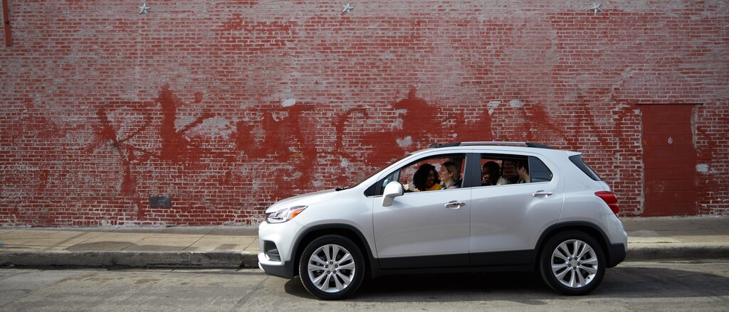 Una Chevrolet Trax plateada con cuatro ocupantes frente a un viejo edificio de ladrillos rojos con graffiti gastados en un lado.