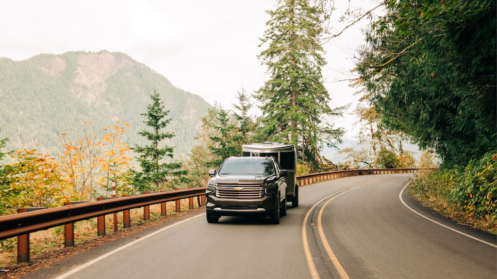 Una Tahoe 2021 negra andando con un remolque Airstream Basecamp X por una carretera de 2 carriles en un área montañosa.