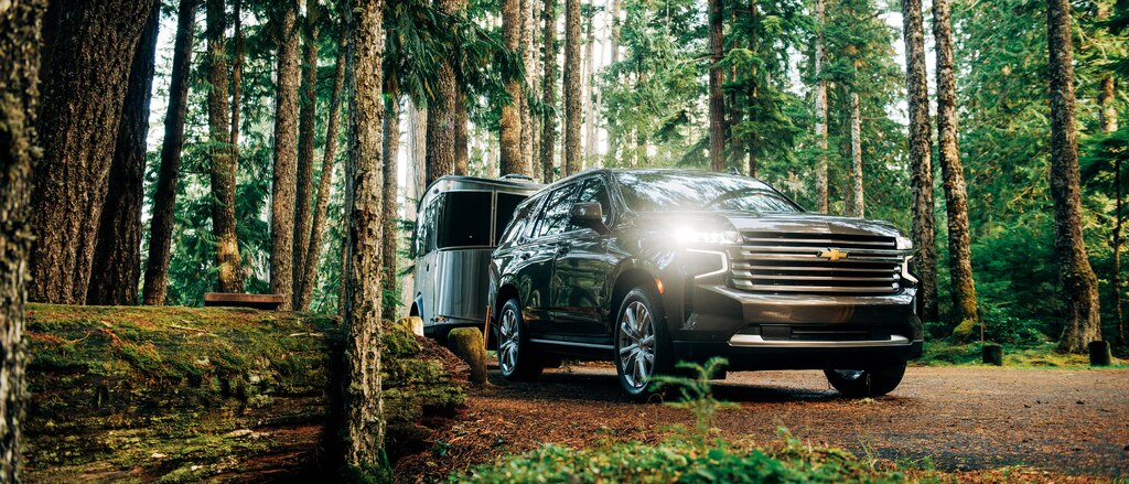 Una Tahoe 2021 negra andando con un remolque Airstream Basecamp X por un bosque.