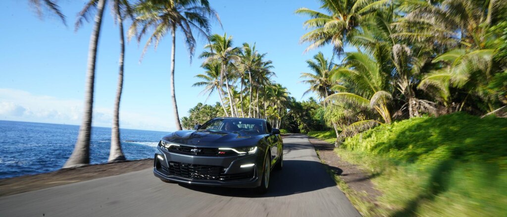 Un Camaro SS 2020 visto desde el frente en un camino pavimentado con palmeras junto al mar.