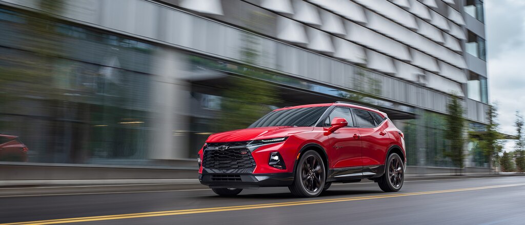 Una Chevy Blazer RS en color Rojo pasando frente a un edificio, vista desde la esquina lateral delantera del conductor.