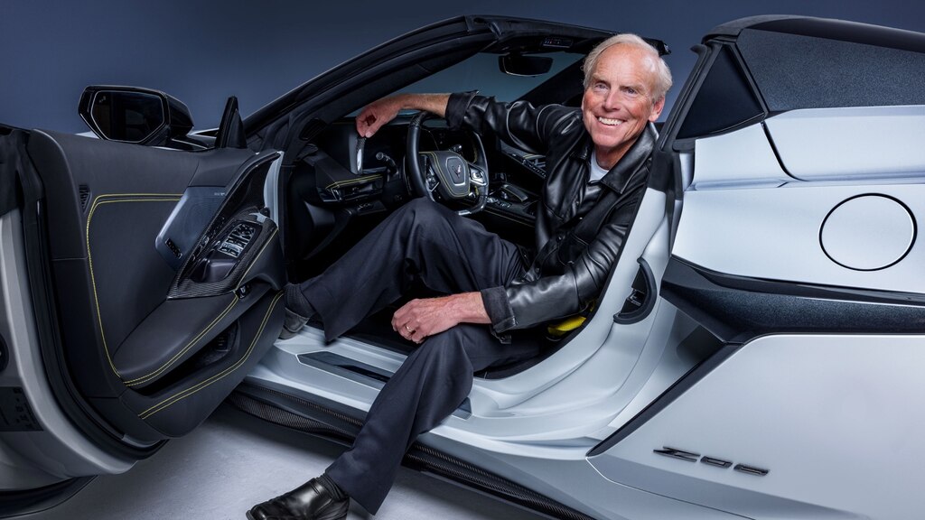 Tadge Juechter sonríe a la cámara desde el asiento del conductor de un Corvette Z06 Blanco. La puerta del conductor está abierta y tiene un pie en el suelo fuera del auto.