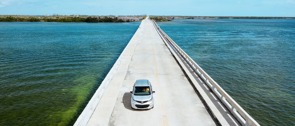 Un Bolt EV color Plata Hielo Metálico que va por una calzada en los Cayos de Florida, con el mar de ambos lados y una isla en el fondo.