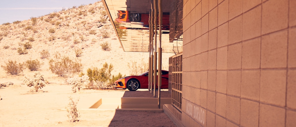 Un Corvette 2020 en Rojo Antorcha estacionado a la sombra junto a una casa contemporánea en el Sudoeste desértico, con un paisaje desértico soleado de fondo.