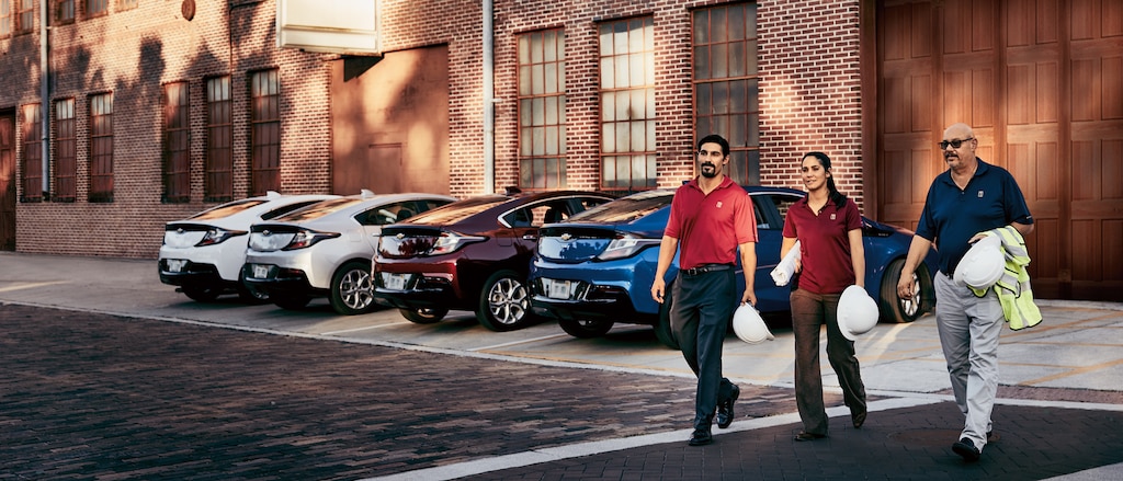 Joe, Anna y Gregory Territo cruzan el estacionamiento enfrente de su flota de Chevy Volts.