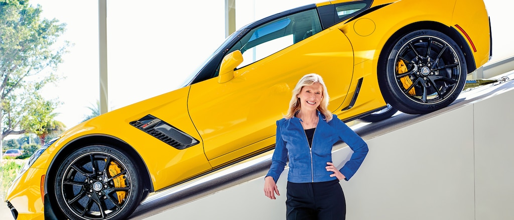 Directora ejecutiva de Hertz, Kathy Marinello, con un Chevrolet Corvette amarillo exhibido en una rampa detrás suyo.