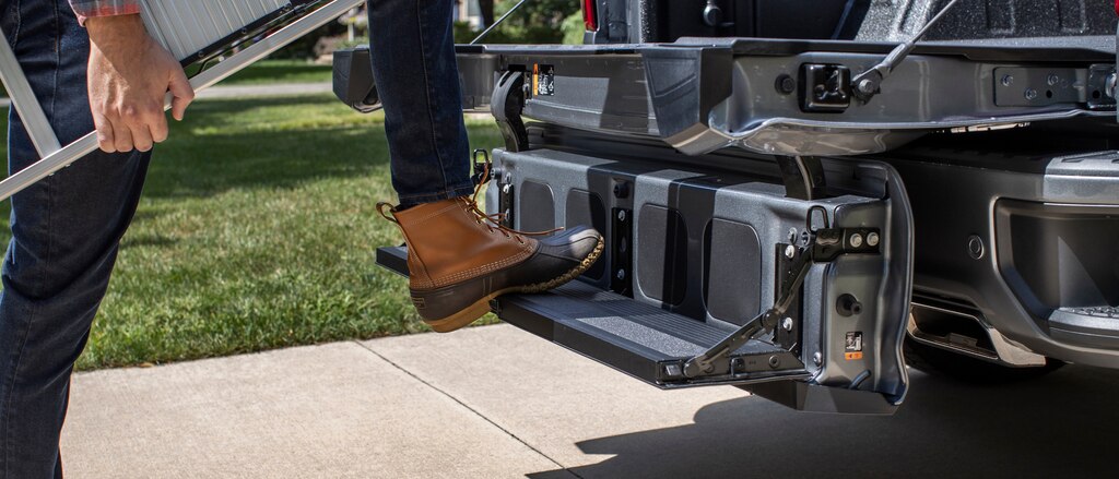 Una persona con botas de trabajo y con una escalera tiene un pie arriba de la puerta trasera Multi-Flex de Silverado configurada como un escalón.