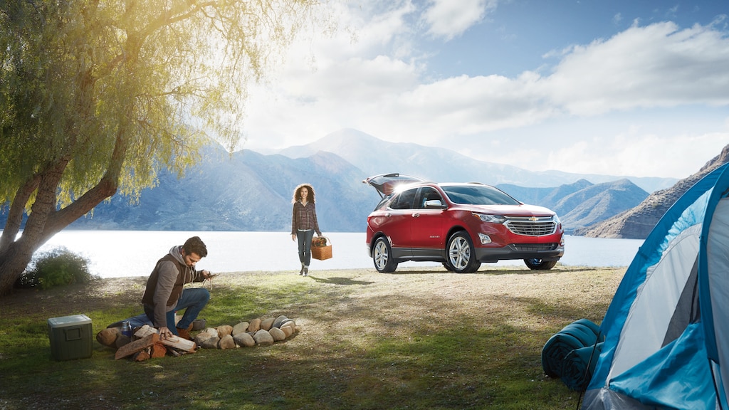 Una pareja se instala en el lugar de camping a la orilla del lago, sacando los equipos de su Chevrolet Equinox.
