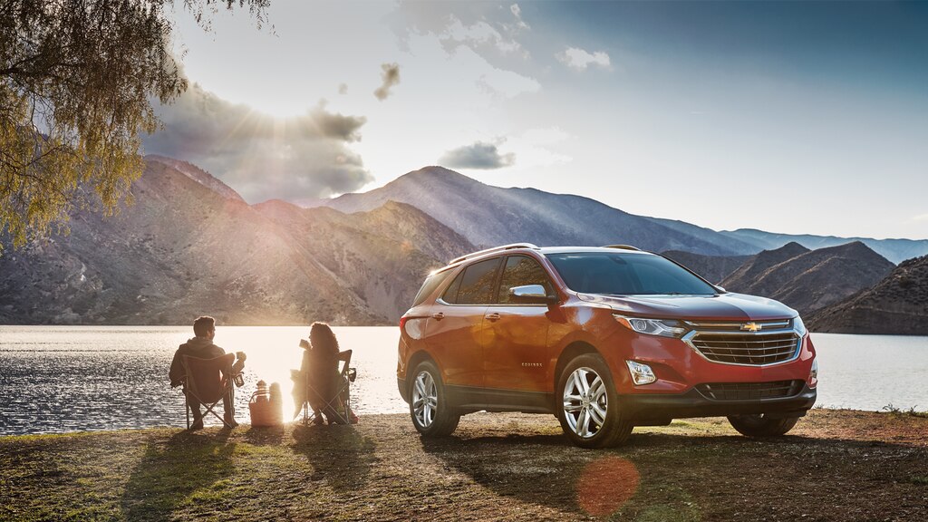 Una pareja disfrutando en la costa de un lago en tumbonas al lado de una Chevrolet Equinox.