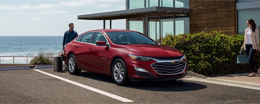 Hombre cargando su equipaje en un Chevy Malibu estacionado cerca del océano