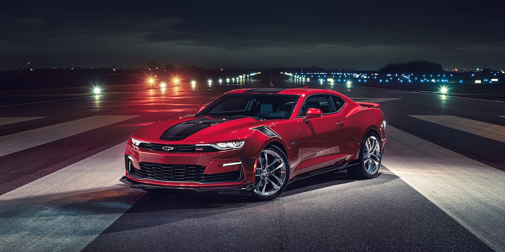 Camaro Rojo con una franja de carreras en Negro estacionado en una carretera sin tráfico por la noche
