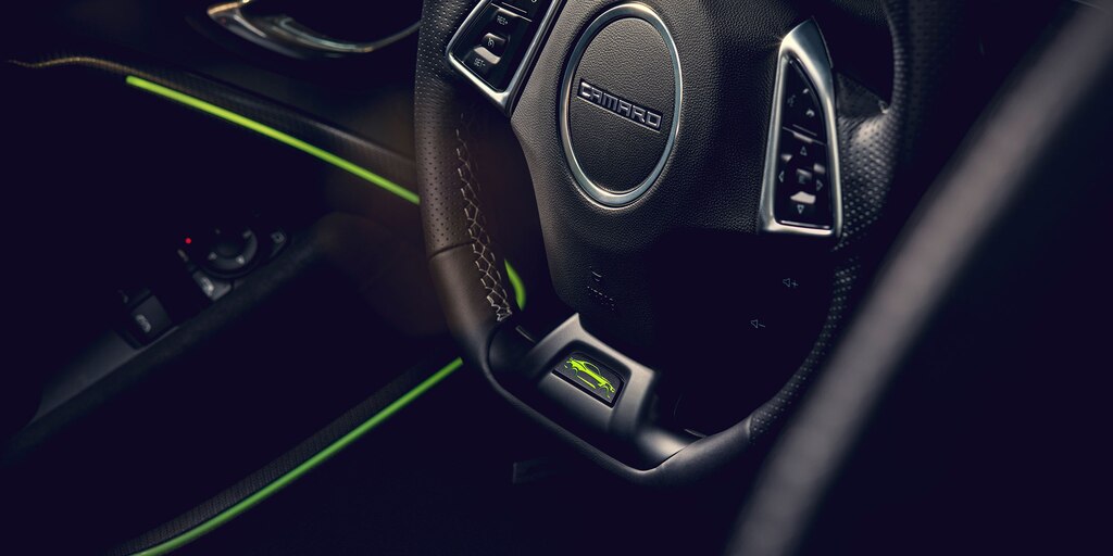 Primer plano del volante en el interior del Camaro, con una luz ambiental en Amarillo