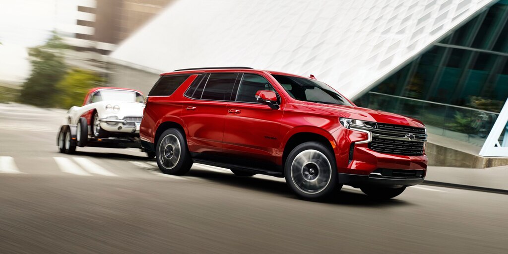 Una Tahoe 2023 en Rojo Radiante Tintcoat girando en una esquina con un auto remolcado por ella