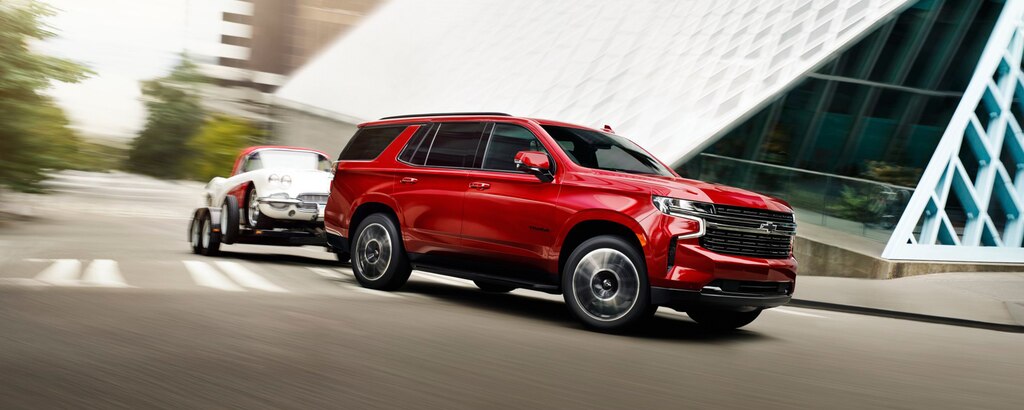 Una Tahoe 2023 en Rojo Radiante Tintcoat girando en una esquina con un auto remolcado por ella