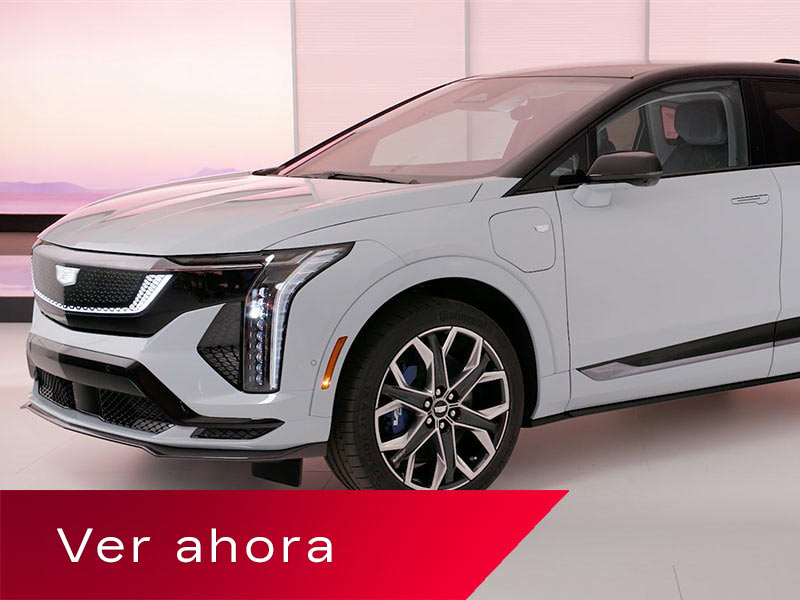 Una Cadillac OPTIQ en Blanco posicionada en un entorno de estudio brillante, con sus distintivos faros delanteros LED verticales y rines de múltiples brazos, arriba de un cartel rojo en el que se lee "Watch Now" (Mirar ahora).
