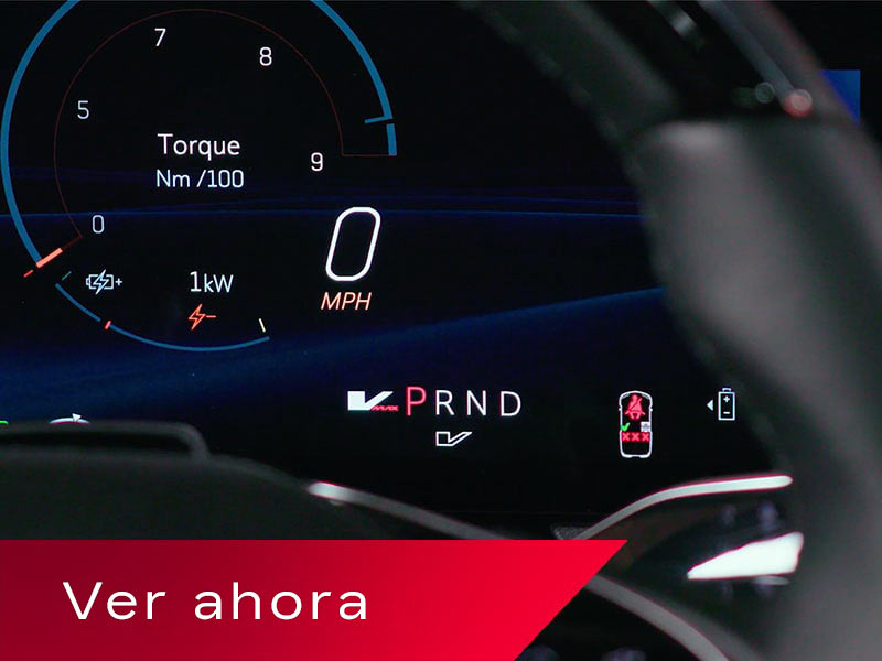 La pantalla digital de la Cadillac OPTIQ, en la que se exhiben el torque, información sobre la velocidad y los indicadores de marcha PRND parcialmente oscurecidos por el volante, arriba de un cartel rojo en el que se lee "Watch Now" (Mirar ahora).